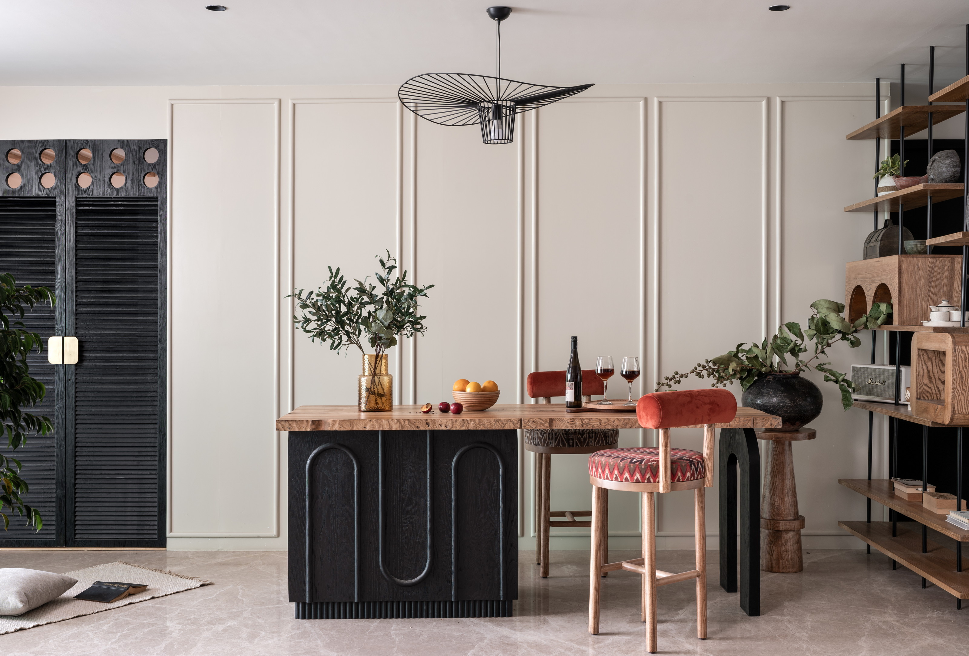 Open dining room with long table, dark doors, wall shelving, plants and pendant light